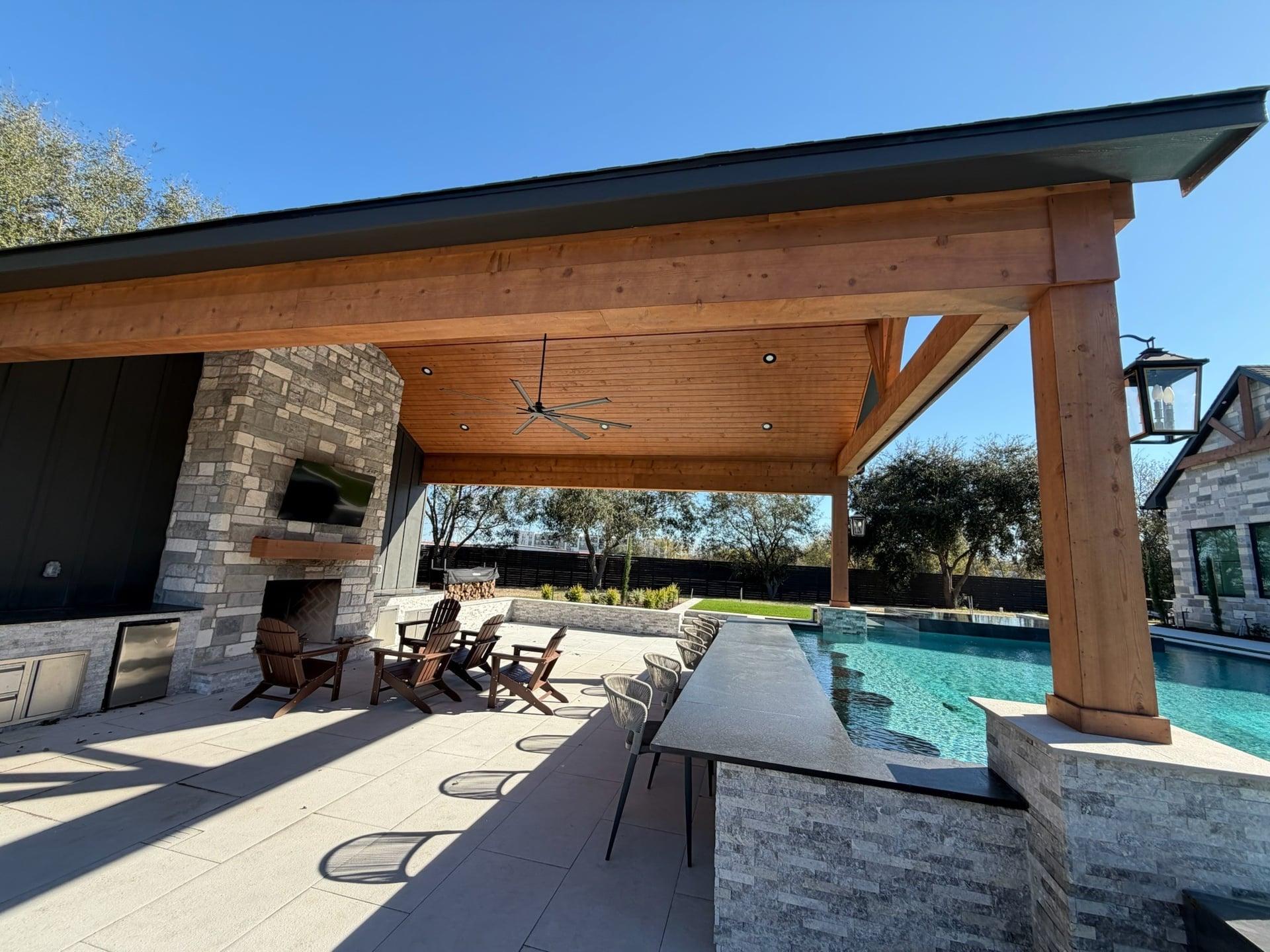 Custom covered patio with stone fireplace, ceiling fan, and bar seating by pool