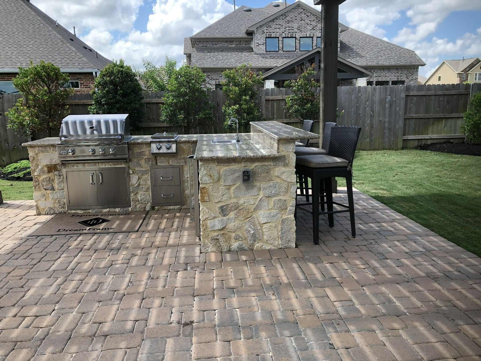 Outdoor kitchen with bar seating on brick paver patio with stone accents