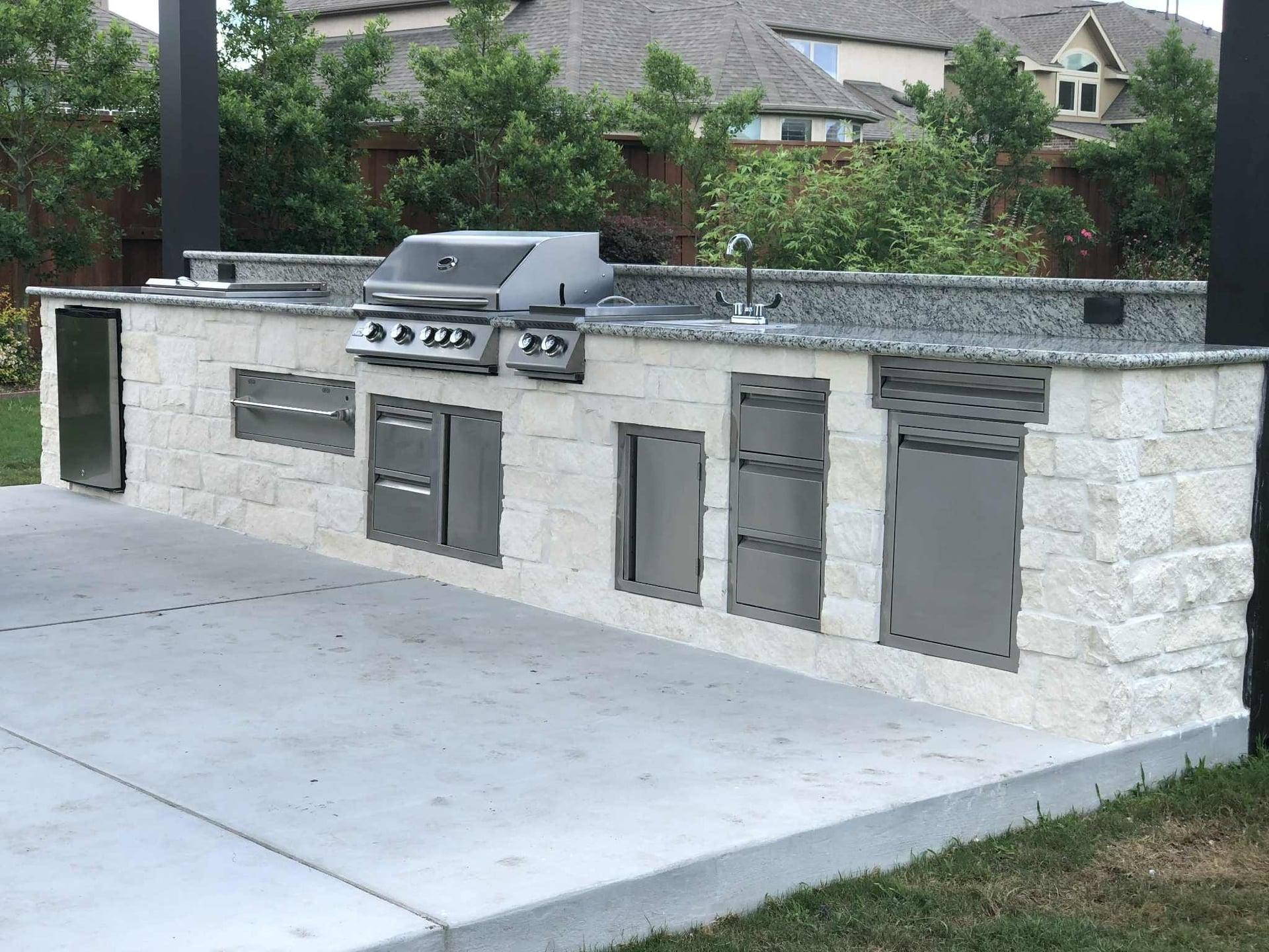 Stone outdoor kitchen with built-in grill and stainless steel appliances on concrete patio