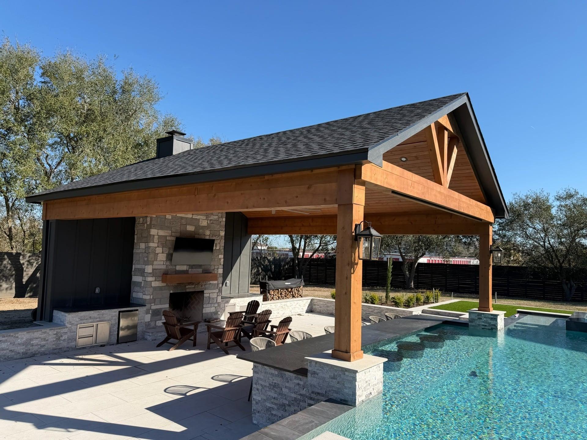 Exterior view of large gable pavilion with stone columns by pool and landscaping